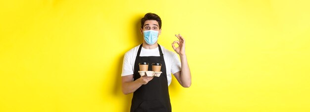 Concept of covid cafe and social distancing barista in medical mask and black apron guarantee safety