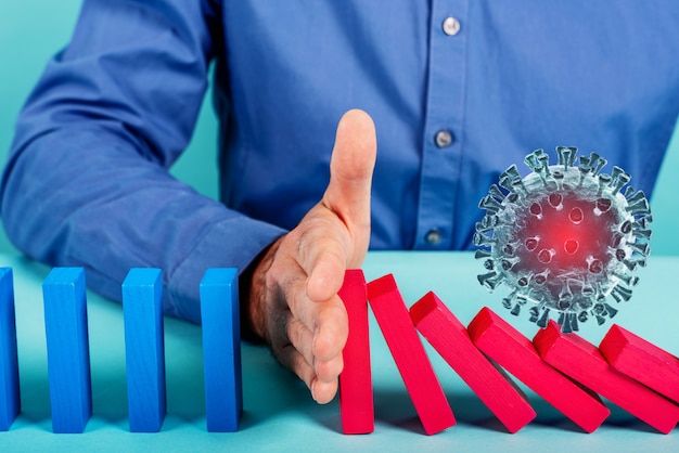 Concept of covid19 coronavirus pandemic with falling chain like a domino game. Contagion and infection progression stopped by a hand of a doctor. Cyan wall