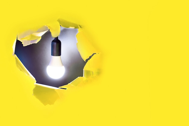 Concept of creative idea. A light bulb shines in a hole of yellow paper