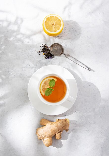 Concept cup of tea with lemon, mint and ginger on a white textured background with morning shadows. Top view image