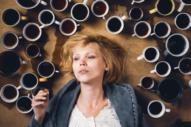 Концепция дедлайна: нужно оставаться жизнерадостной Женщина в окружении множества чашек кофе