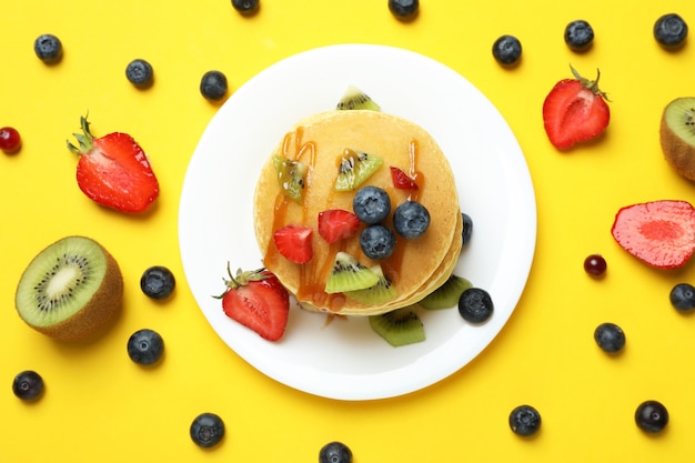 Concept of delicious dessert with pancakes on yellow background