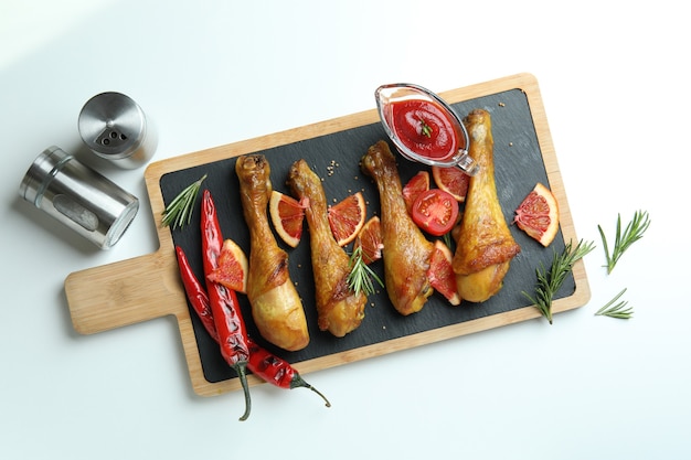 Concept of delicious eating with board of roast chicken drumsticks on white background