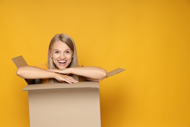 Photo concept of delivery and gift young woman in box on yellow background