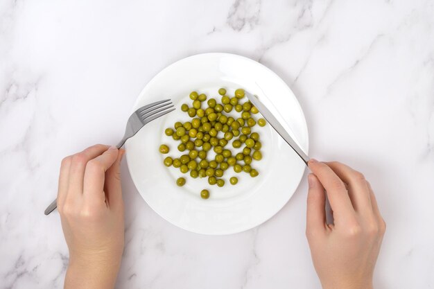 The concept of diet and weight loss Women's hands with a fork and a table knife over a plate of green peas