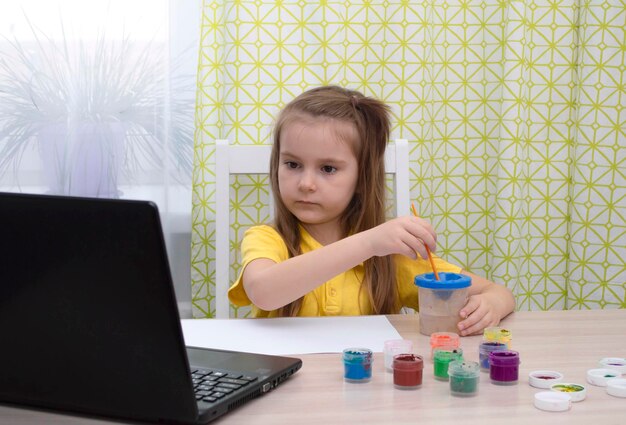 Concetto di educazione a distanza. la ragazza impara a disegnare online durante l'autoisolamento. studia in linea. lezione di disegno con laptop. disegna un'immagine con i colori. la vita nell'era digitale. di nuovo a scuola.