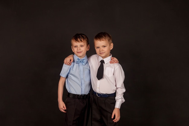 Concept of education, upbringing, male friendship and fraternity. Two little stylish boys brothers and friends, hugging and happy together, on black background. Portrait of 2 guys towards same goal