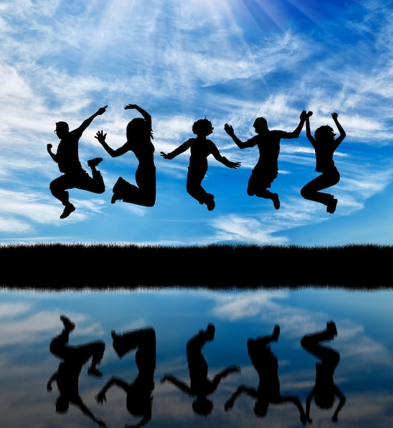 Concept of emotion. Silhouette of a happy group of people jumping against the sky