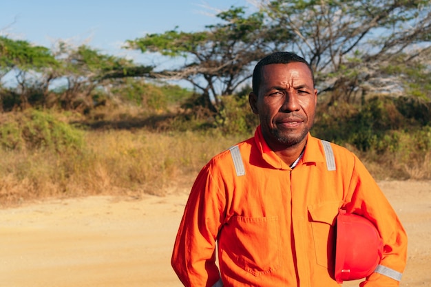 Concept of engineer or technician. Black Male mechanic in orange uniform with helmet on his arm.