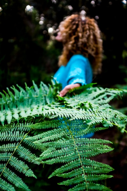 Foto concetto di ambiente e salvare il pianeta terra con primo piano di foglia verde tropicale e donna sullo sfondo - la natura e la cura della foresta all'aperto per le persone che amano la vita all'aria aperta