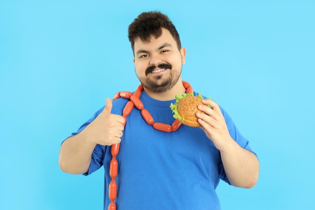 Concept of excess weight fat guy with food on blue background