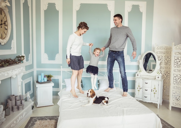 Concept of family happiness: loving parents playing with baby daughter on bed in bedroom