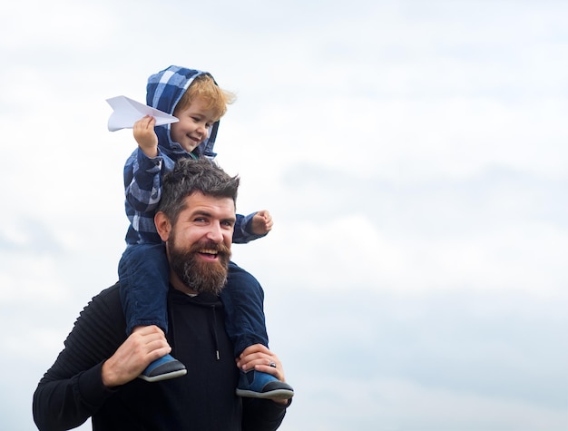 Concept of Fathers day Father and son together Childhood Happy child playing with toy paper plane against summer sky background