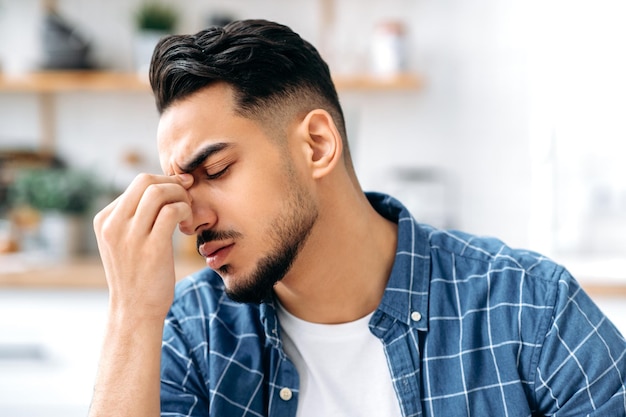 The concept of fatigue migraine headache closeup of a tired\
exhausted indian or arabian man massaging the bridge of his nose\
having a headache migraine closed his head need rest