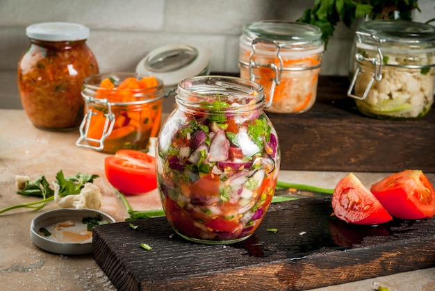 Concept of a fermented meal. Home canned food and billets. Vegan food. Vegetables. Cans of canned salsa, sauerkraut, marinated carrots, kimchi and cauliflower broccoli. Home kitchen table.  copyspace