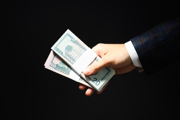 Concept of financials businessman hand holds dollars on dark background