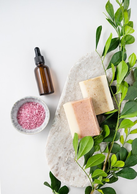 Concept flat lay of facial and body care cosmetics with pink sea salt soap and cream on white background with brunch Top view and copy space Vertcal orientation