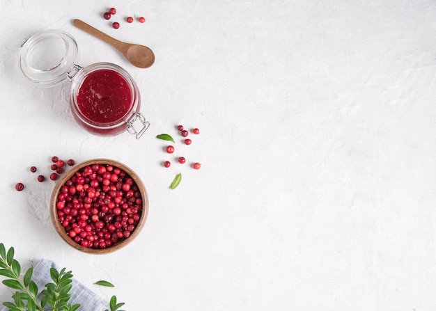 Concept flat lay with homemade lingonberry jam and forest cowberry in bowl on white table