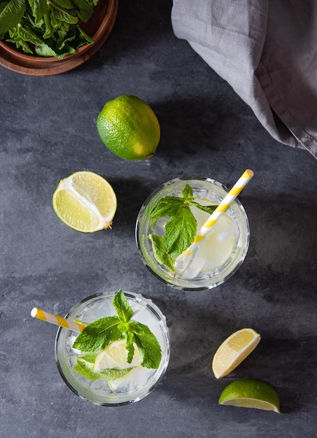 Concept flatlay mojito drink Two glasses of lime lemonade with lime slices and mint on dark gray background Top view image