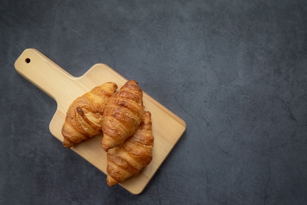 Concept food. Delicious fresh croissants on a wooden board. View from above and a dark background.