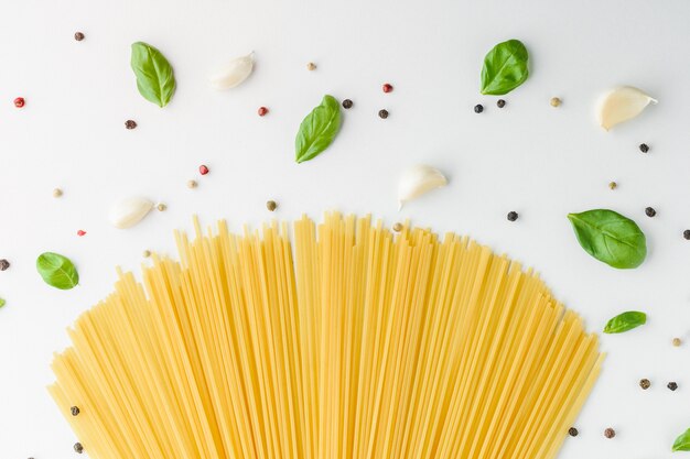 Alimento di concetto con pasta, basilico, aglio e pepe su una priorità bassa bianca