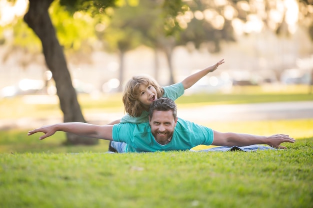 Concept of friendly family Father lying on grass with excited happy little child son on shoulder Carefree two man generations family