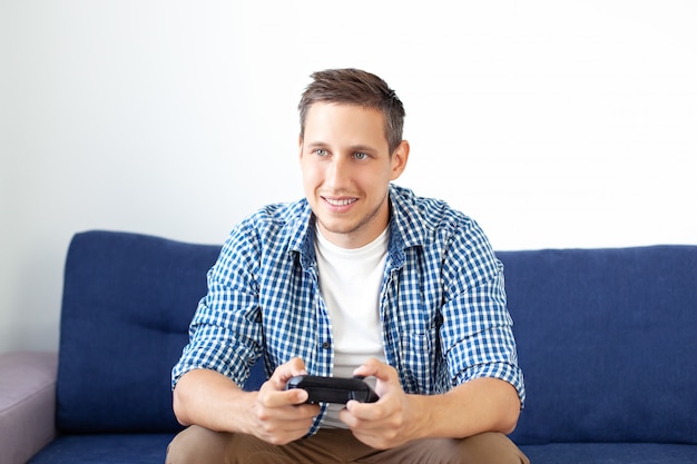 Photo the concept of the game. the guy is playing a video game with a joystick at home. a smiling man in a shirt, sitting on the couch, plays a video game with a joystick. computer games competition. gamer.