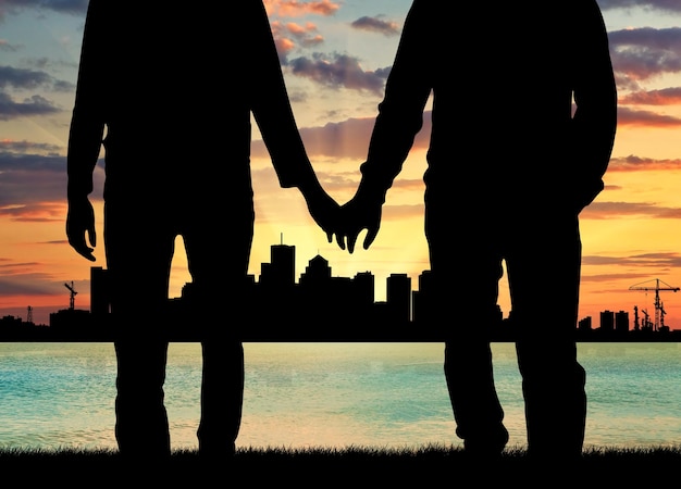 Concept of gay people. Silhouette happy gay men holding hands against the evening sea sunset and the city