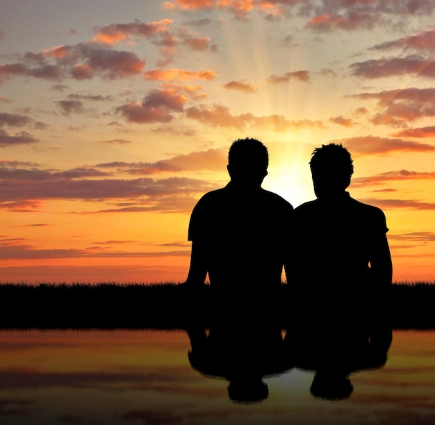 Concept of gay people. Silhouette of two gay holidaymakers near the river at sunset