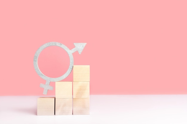 Концепция макета гендерного равенства на розовом фоне с местом для текста Символ гендерного равенства серебристого цвета стоит на деревянных кубиках, расположенных в виде пирамидальной лестницы