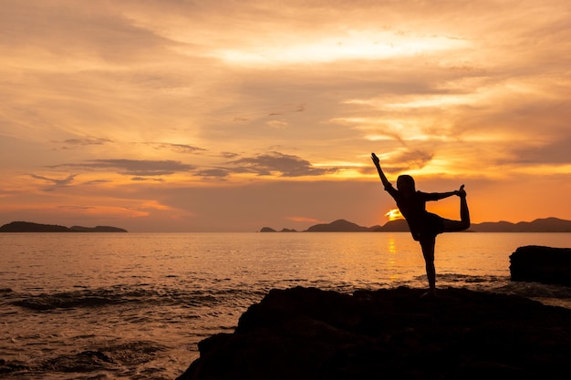 Concept gezond en ontspannend met silhouet van jonge vrouw die yoga beoefent op de rots