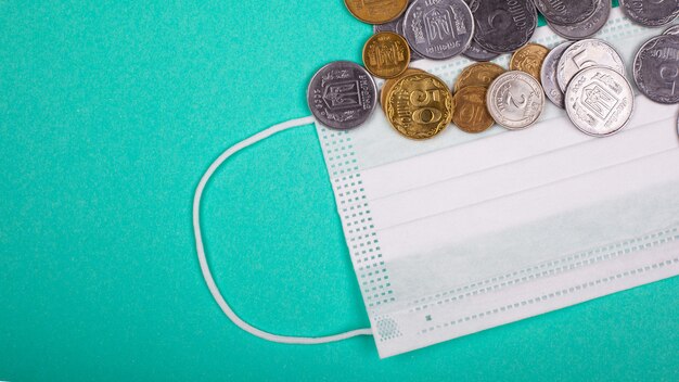 The concept of the global medical crisis in connection with the coronavirus pandemic. protective medical mask and coins on a blue-green background.