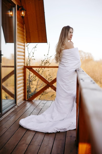 Concept good morning blonde woman on the balcony covered with white duvet morning woman portrait