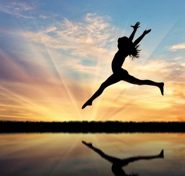 Concept of happiness and freedom. Silhouette of happy woman jumping at sunset and reflection in water