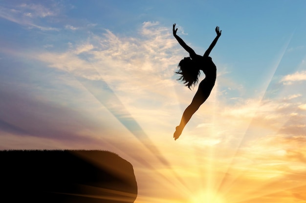 Concept of happiness and freedom. Silhouette of happy woman jumping at sunset