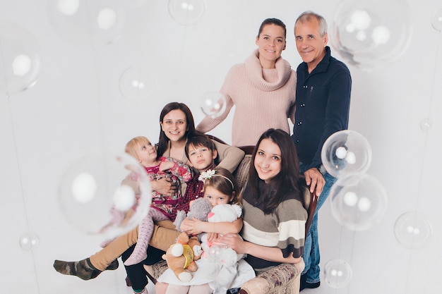 Concept of happy childhood, family, love - group of people on a white background: adults and children with toys sitting on the same couch