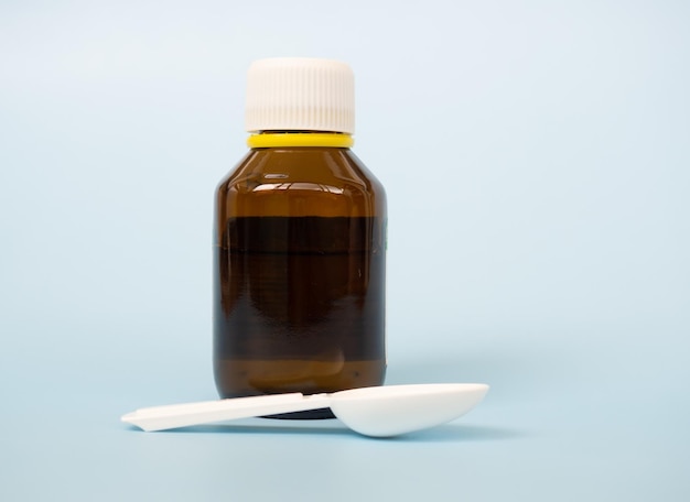 the concept of health care treatment and medicine a bottle of medicines or antipyretic syrup and a measuring spoon children's cough syrup on a blue background