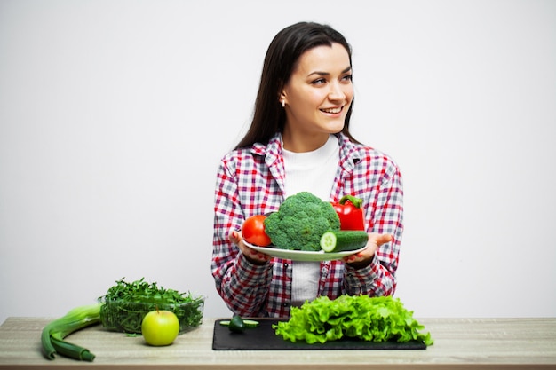 背景の白い壁に野菜を保持している健康的な食事とダイエットの女の子の概念