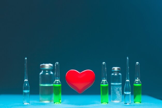 The concept of a healthy heart. Red volumetric heart on the background of ampoules with medicines.