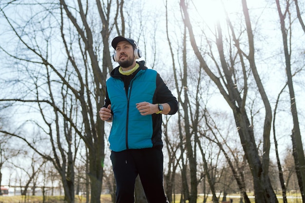 The concept of healthy living an athletic man jogs through the park wearing wireless headphones