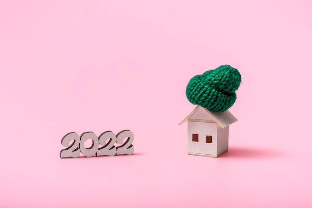 The concept of the heating season 2022. On a pink background, a wooden house in a green hat close up with copy space