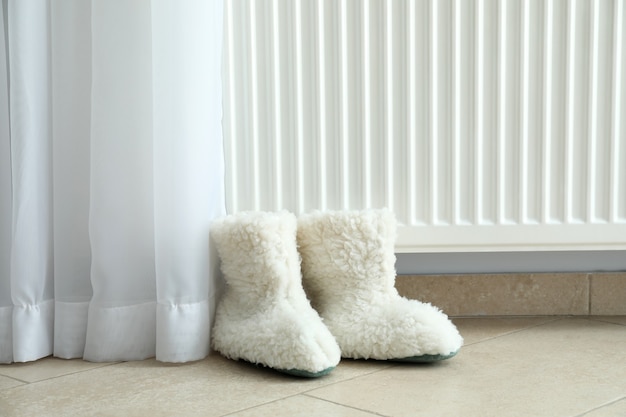 Photo concept of heating season with knitted boots near radiator.