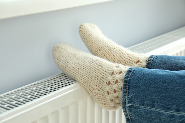 Concept of heating season with legs in knitted boots on radiator.