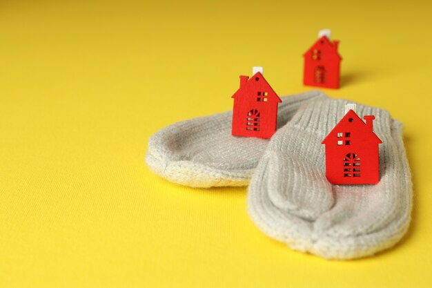 Concept of heating season with mittens and red houses on yellow background.