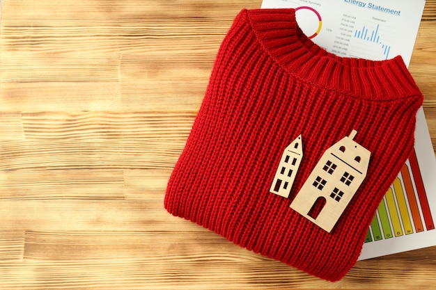 Concept of heating season with red sweater on wooden table.