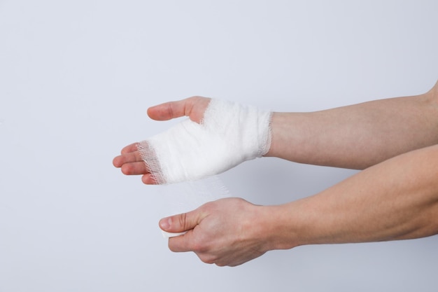 Concept of help during an injury man wrapping hand in bandage on white background