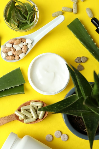 Concept of herb pills and cosmetics with aloe on yellow background