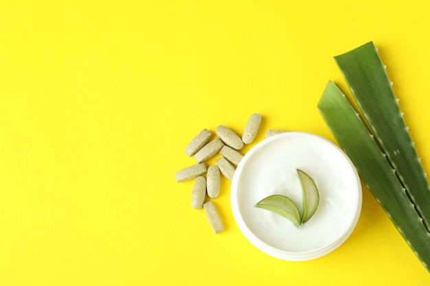 Concept of herb pills and cosmetics with aloe on yellow background