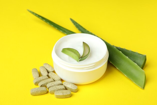 Concept of herb pills and cosmetics with aloe on yellow background