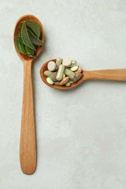 Concept of herb pills with aloe slices on white textured background